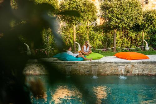 a woman and a child sitting next to a swimming pool at PALAZZO DEL CAPITANO Wellness & Relais - Luxury Borgo Capitano Collection in San Quirico dʼOrcia