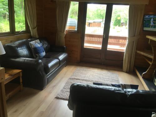 a living room with black leather couches and a porch at Chalet 2 in Tyndrum