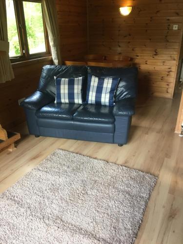 a black leather couch in a living room with a rug at Chalet 2 in Tyndrum