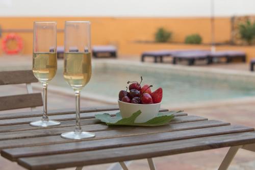 two glasses of wine and a bowl of fruit on a table near a pool at Casa da Falfeira B&B in Lagos
