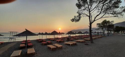 a beach with chairs and umbrellas and the sunset at Nada SeaView Apartment in Shëngjin