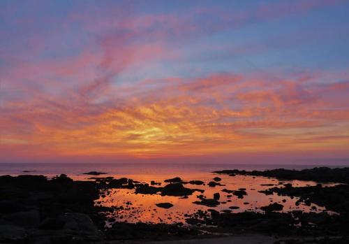 um pôr-do-sol sobre o oceano com pedras na água em Alumar Apartamentos Muxia em Muxía