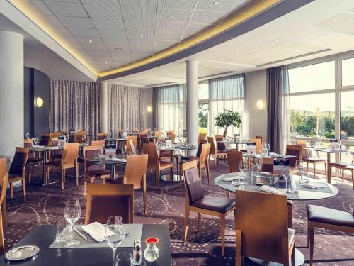 a dining room with tables and chairs and windows at Mercure Compiègne Sud in Compiègne