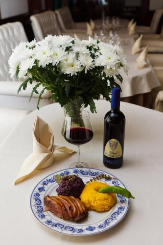 a plate of food and a bottle of wine and a vase of flowers at Hotel Roman by Dumbrava Business Resort in Roman