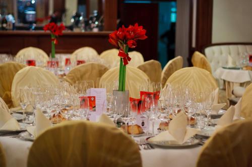 a table with glasses and a red flower in a vase at Hotel Roman by Dumbrava Business Resort in Roman