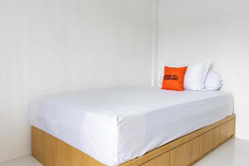 a bed with white sheets and an orange pillow on it at RedDoorz Plus near Soekarno Hatta Airport Taman Mahkota in Tangerang