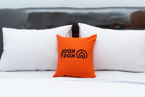 an orange pillow sitting on a bed with three white pillows at RedDoorz Plus near Soekarno Hatta Airport Taman Mahkota in Tangerang