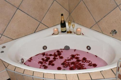 a bath tub filled with red debris with wine bottles and candles at Batter Boys Guest House in Pretoria