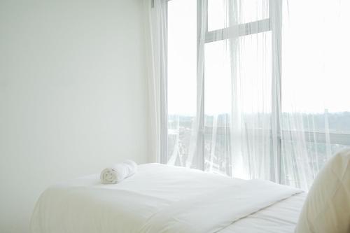 a white bedroom with a bed and a large window at New Furnished 2BR Apartment at Serpong M-Town Residence By Travelio in Tangerang