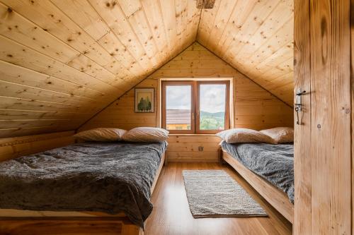 two beds in a wooden cabin with a window at Chaty Jak Dawniej in Wołkowyja