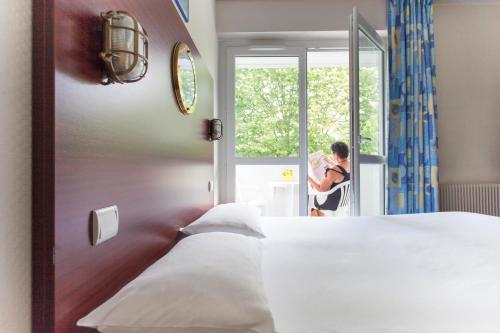 a person standing in a bedroom looking out the window at Hôtel Les Gens de Mer La Rochelle by Popinns** in La Rochelle