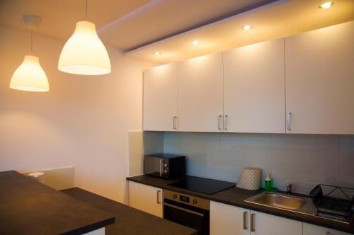 a kitchen with white cabinets and a sink and two lights at Apartament Mirek in Łódź