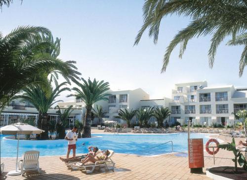 two people sitting in chairs by the swimming pool at a resort at Hotel Riu Oliva Beach Resort - All Inclusive in Corralejo