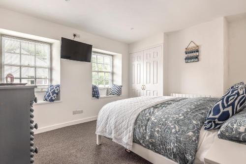 a white bedroom with a bed and two windows at Lime Kiln Cottage, Pentewan, Cornwall in Pentewan