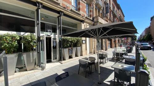een patio met tafels en stoelen en een parasol bij ibis Toulouse Gare Matabiau in Toulouse