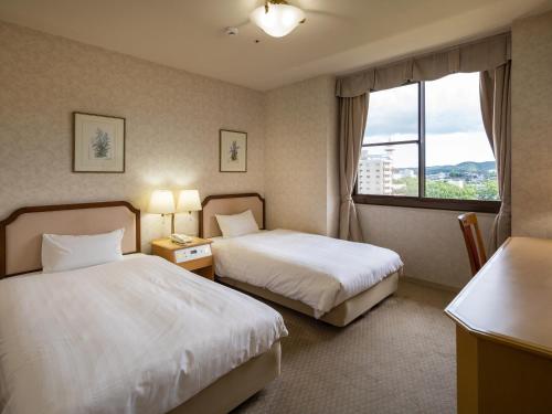 a hotel room with two beds and a window at Hotel Flags Isahaya Nagasaki in Isahaya