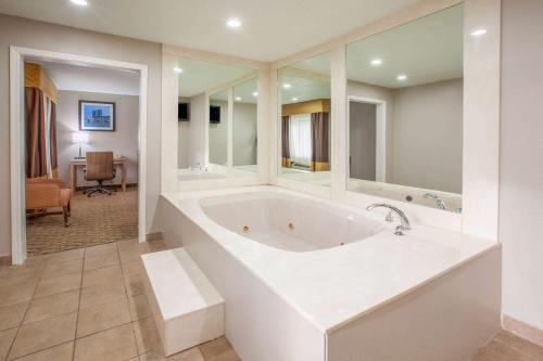 une grande salle de bains blanche avec baignoire et une chambre dans l'établissement Baymont by Wyndham Grand Rapids Airport, à Grand Rapids