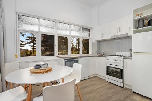 a white kitchen with a white table and chairs at Bayview Apartments Glenelg in Adelaide