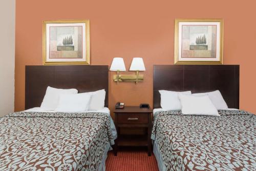 two beds in a hotel room with orange walls at Days Inn & Suites by Wyndham Des Moines Airport in Des Moines