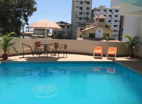 een tafel met stoelen en een parasol naast een zwembad bij Hotel Arena Blanca in Salinas