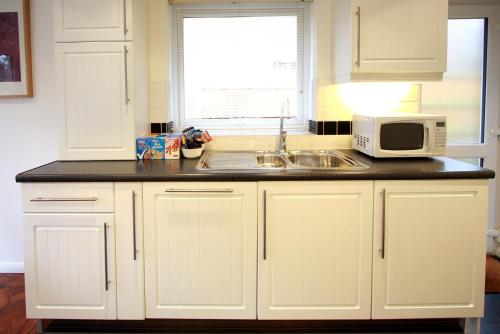 a kitchen with white cabinets and a sink and a microwave at Abacus Bed and Breakfast, Blackwater, Hampshire in Camberley
