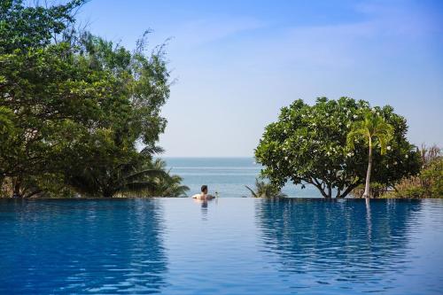 a man in a infinity pool with the ocean in the background at Victoria Phan Thiet Beach Resort & Spa in Mui Ne