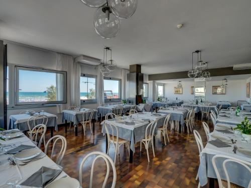 a dining room with white tables and chairs and windows at Hotel Europa in Senigallia
