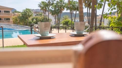 two cups on a wooden table next to a pool at Mon Port Hotel & Spa in Port d’Andratx