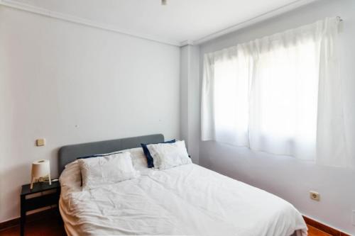 een slaapkamer met een bed met witte lakens en een raam bij ¡Nuevo! Apartamento para 4 en playa de la Concha en Suances in Suances