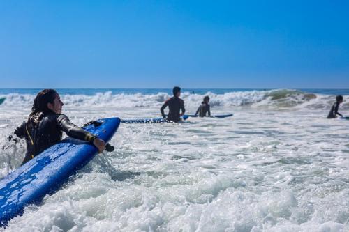 a woman holding a blue surfboard in the water at The Lunar Surf House in Tamraght Ouzdar