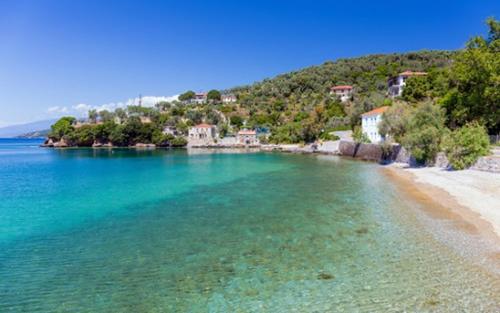 a beach with turquoise water and trees and houses at Aktaion in Milína