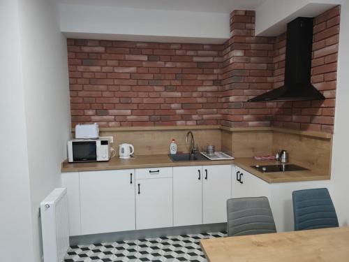 una cocina con armarios blancos y una pared de ladrillo en Androméda Apartman, en Sárvár