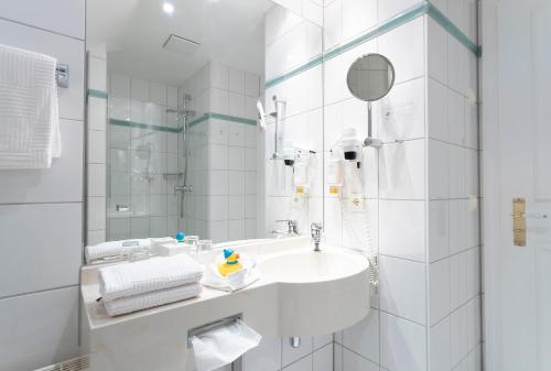 a white bathroom with a sink and a mirror at Strandhotel Sylt Westerland in Westerland (Sylt)