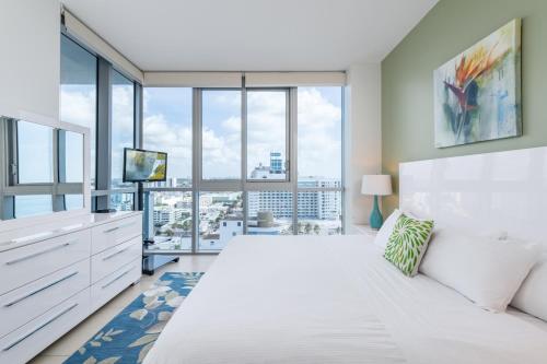 a bedroom with a large white bed and large windows at Bluebird Suites Monte Carlo Miami Beach in Miami Beach