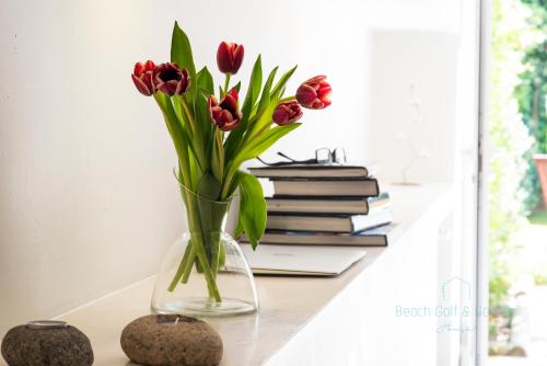 a vase with red tulips sitting on a table with books at Beach Golf & Garden House in Arcozelo