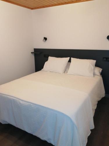uma cama com lençóis brancos e almofadas num quarto em Apartamento A Fabrica em Santiago de Compostela