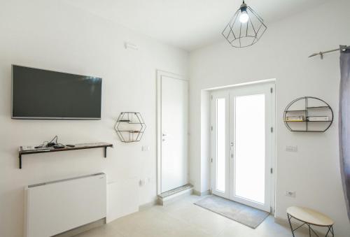 a white living room with a flat screen tv on the wall at Tatta & Nanna Apartment in Oliena