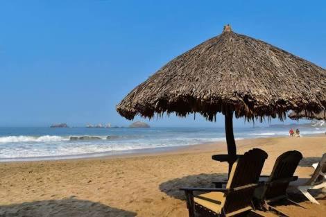two chairs and an umbrella on a beach at VILLA PARA 8p 6A 2M dentro del HOTEL a un costado del Krystal IXTAPA cuenta con playa y WIFI in Ixtapa