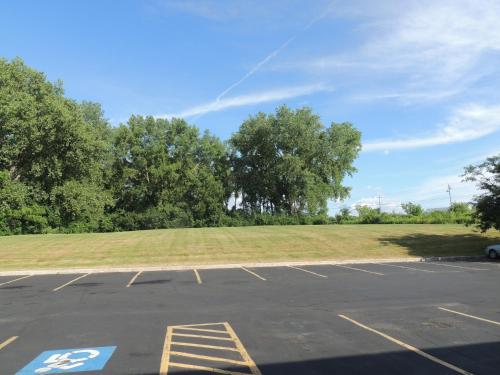 a parking lot with a grass field and trees at Quality Inn & Suites Syracuse Fairgrounds in Liverpool