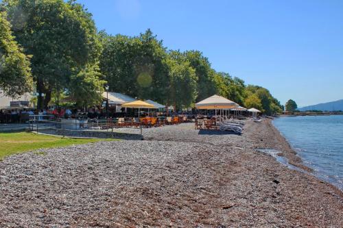 a beach with tables and umbrellas on the water at Vallia Suites - Luxury Penthouse in Nafpaktos