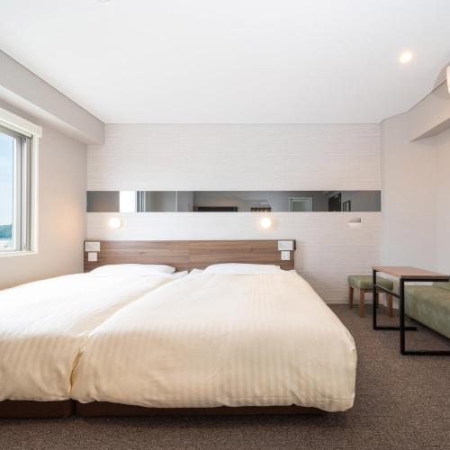 a bedroom with a large white bed and a couch at Super Hotel Beppu Ekimae in Beppu