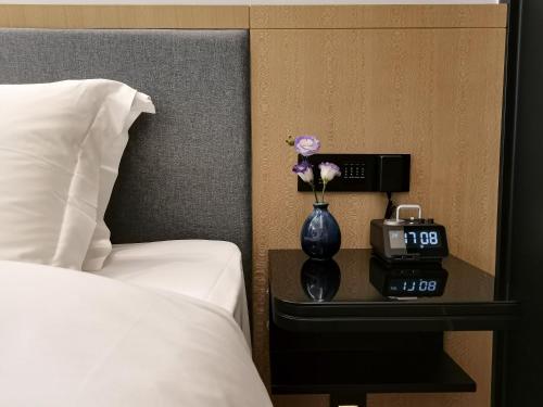 a clock and a vase with flowers on a table next to a bed at Paco Hotel BeiJing Road Metro Guangzhou-Free Shuttle Bus For Canton Fair in Guangzhou