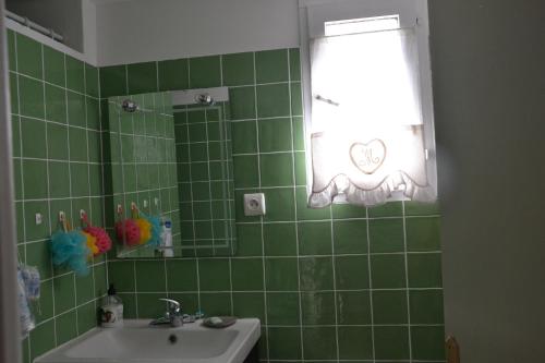 - une salle de bains carrelée de vert avec lavabo et fenêtre dans l'établissement Le patio de Torreilles-Plage, à Torreilles