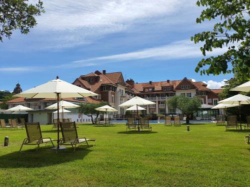 a grassy area with tables, chairs and umbrellas at Gran Hotel Balneario De Puente Viesgo in Puente Viesgo