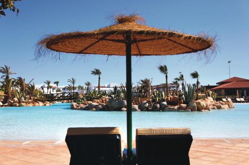 an umbrella and two chairs in front of a swimming pool at Hotel Riu Tikida Dunas - All inclusive in Agadir