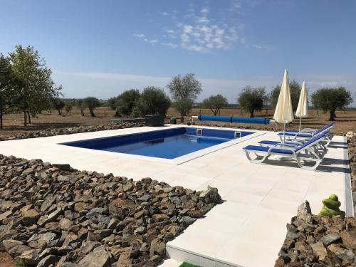 a swimming pool with a rock wall and two chairs and umbrellas at Horta da Rosa - Adults Only in Alvito