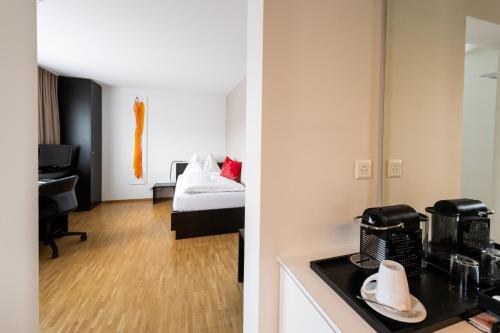a room with a kitchen and a room with a bed at Hotel Bauernhof - Self Check-In Hotel in Rotkreuz