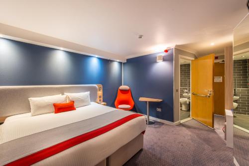a hotel room with a bed and a red chair at Holiday Inn Express Strathclyde Park M74, Jct 5 by IHG in Motherwell