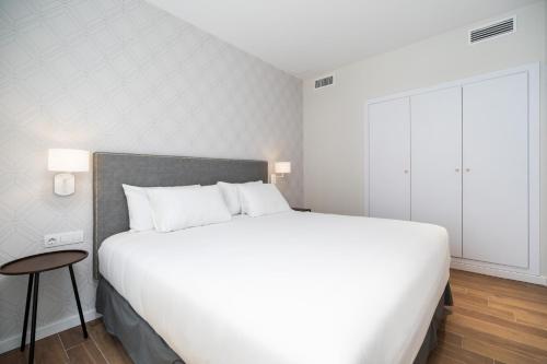 a bedroom with a large white bed and a stool at Tandem Puerto Chico in Cádiz