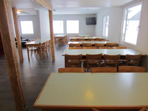 a dining room with tables and chairs and windows at Mountain Lodge Backpackercamp in Lenk